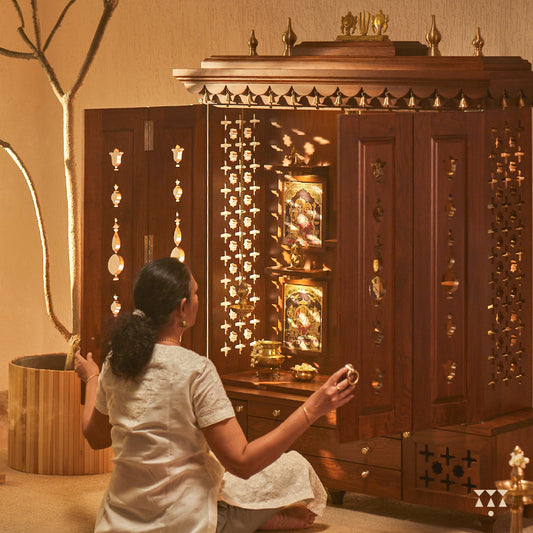A woman praying in front of a mandir with, pure brass bells, accessories, cutwork designs and storage, tinted in an almond brown color