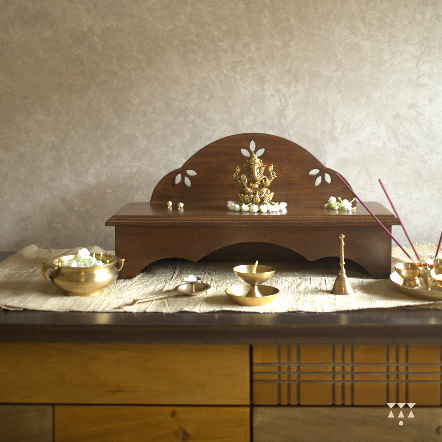 Wooden pooja platform placed on a table with religious brass decor.