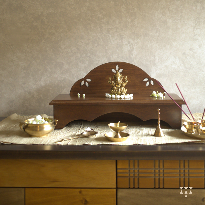 Wooden pooja platform placed on a table with religious brass decor.