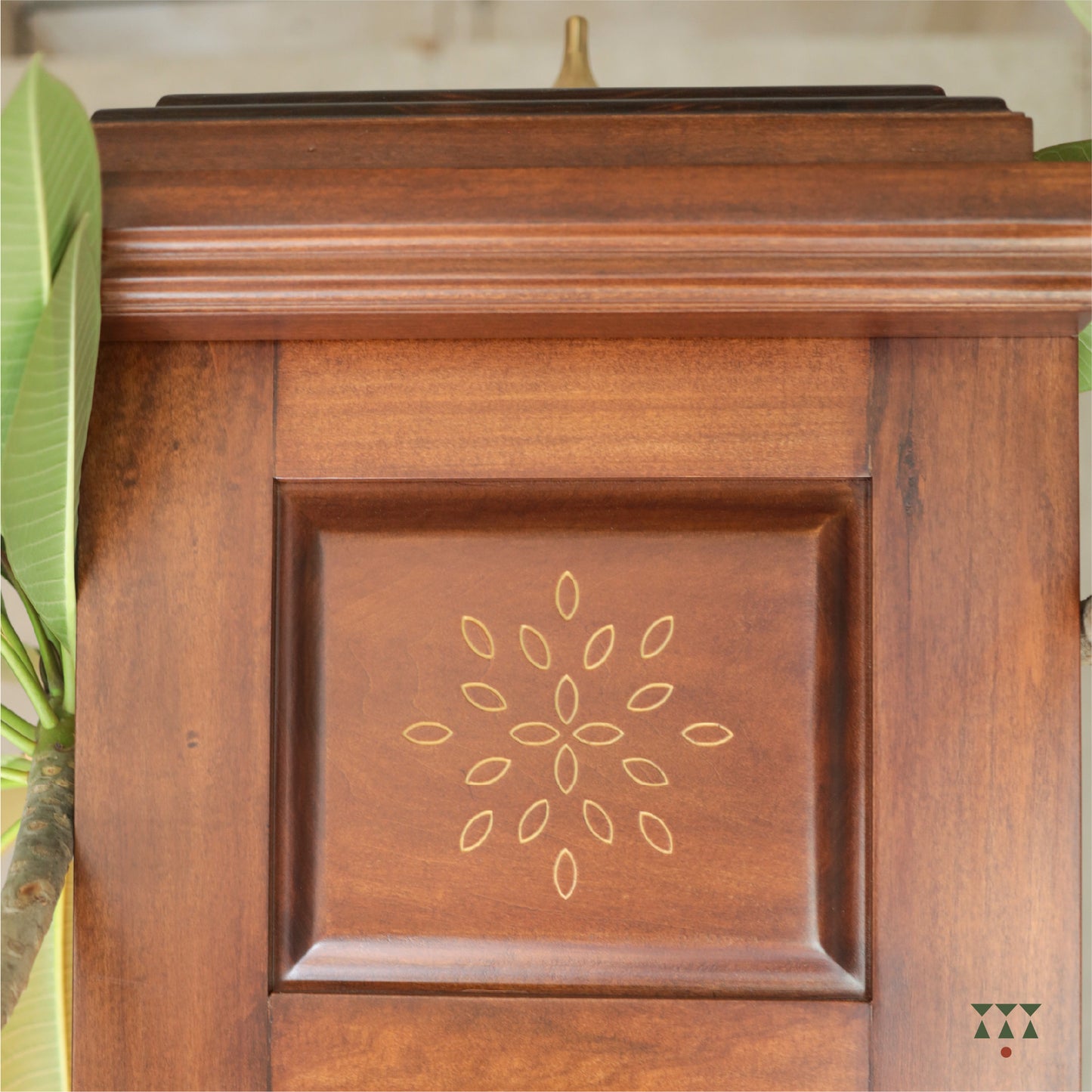Wooden pooja mandir  with decorative engraving design, surrounded by green leaves.