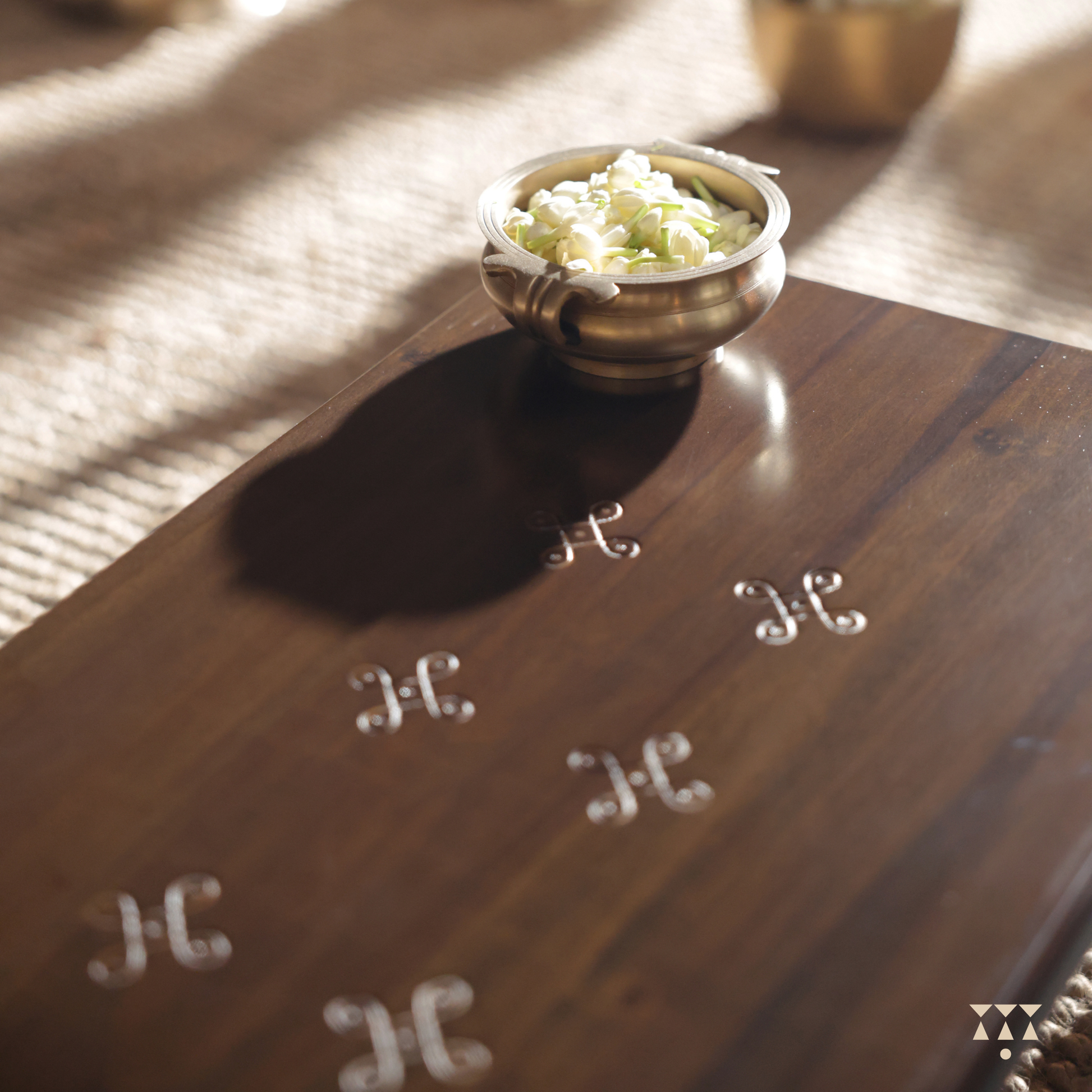 Close up of wooden table with Kolam pattern on it and a brass bowl with mogra in it.